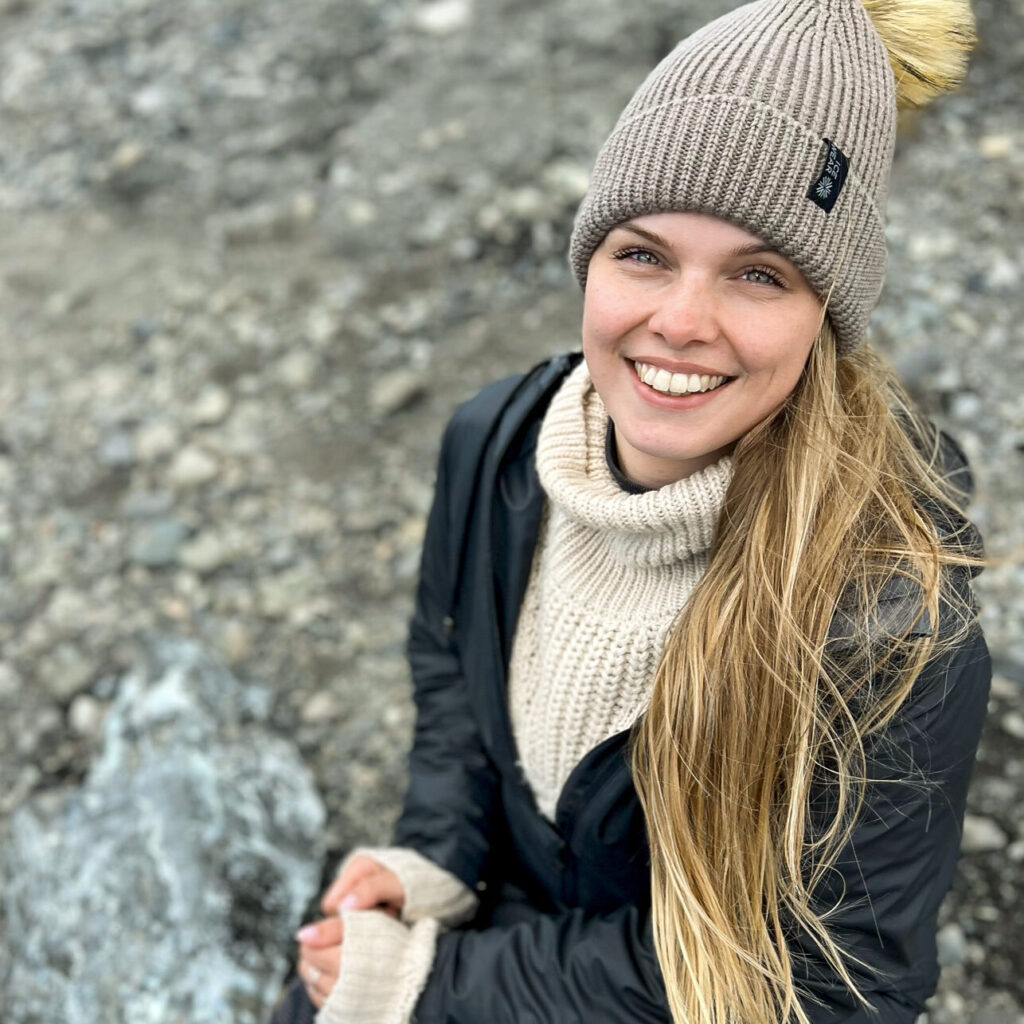 Photo of woman on a sitting on a rocky beach looking up to the camera.